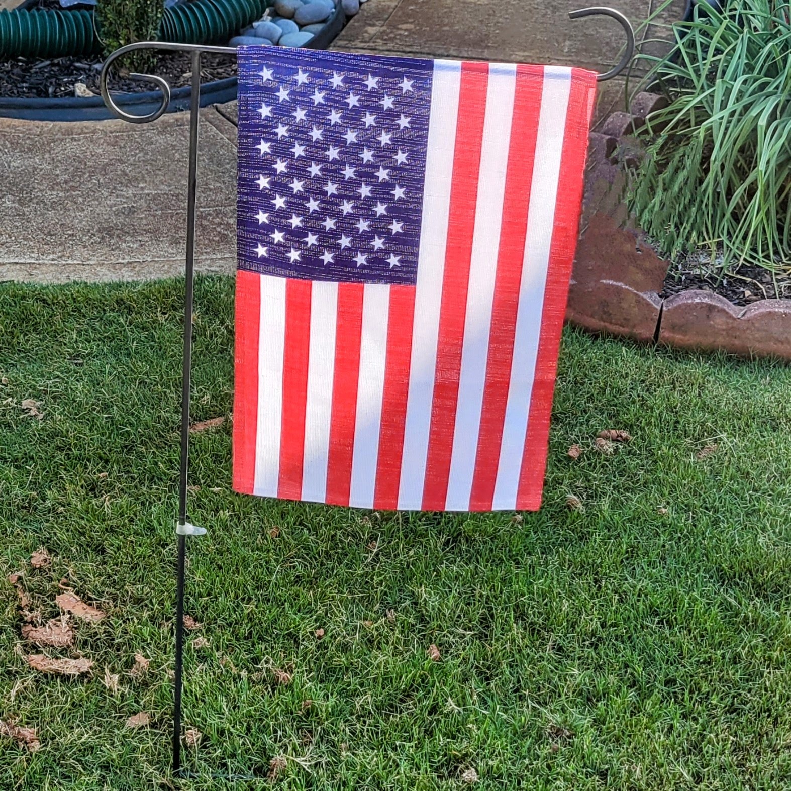 A small American flag hanging vertically in a garden.